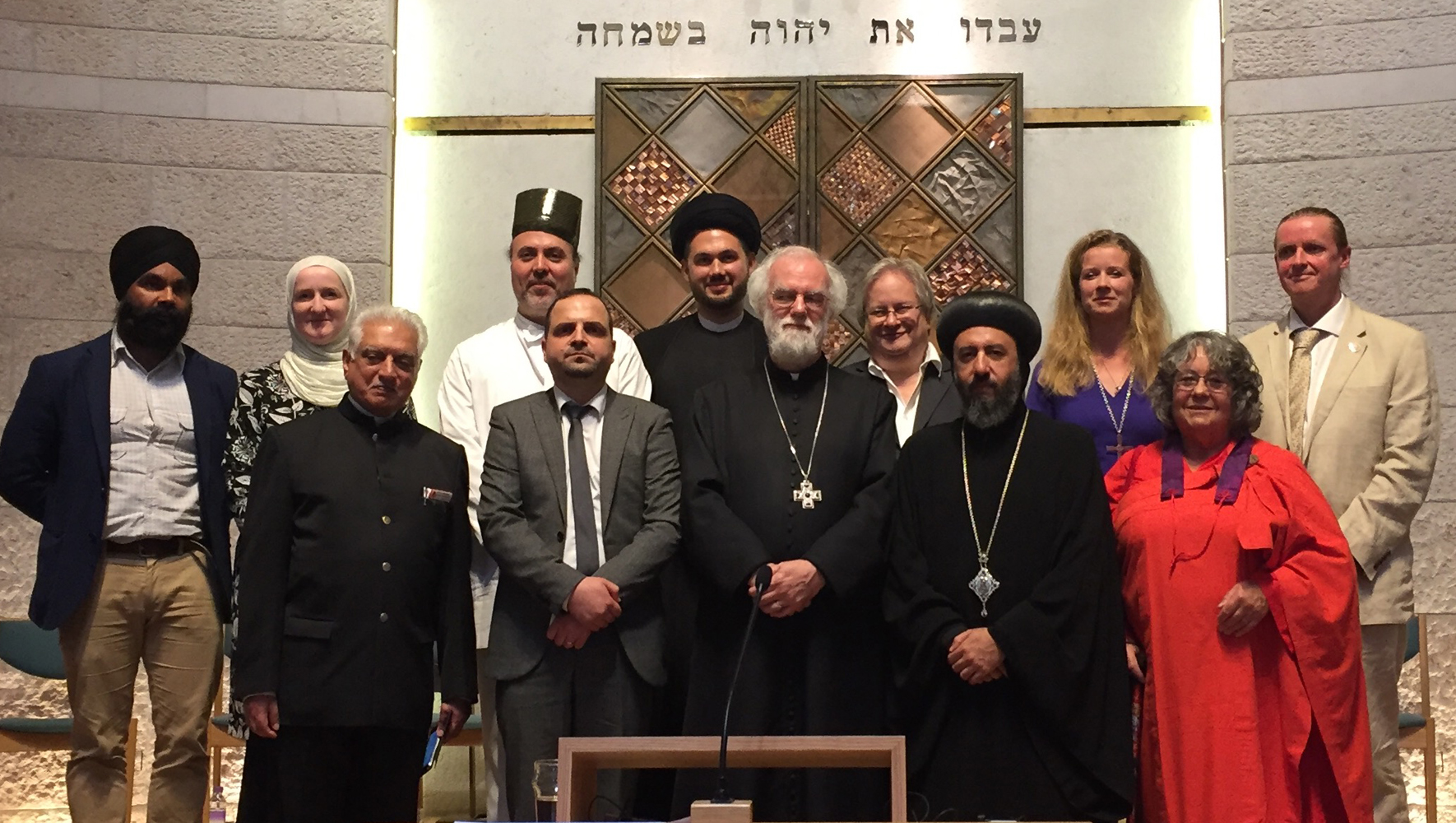 A group of twelve faith leaders are standing in front of the ark in a synagogue.