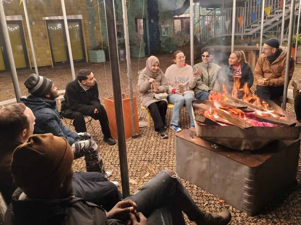 Photo shows a group of people set in a semi-circle, in front of a log fire.