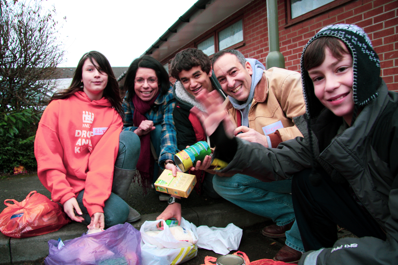 A family of volunteers at the New North London synagogue asylum-drop in centre are smiling at the camera. They are holding food which has been donated.