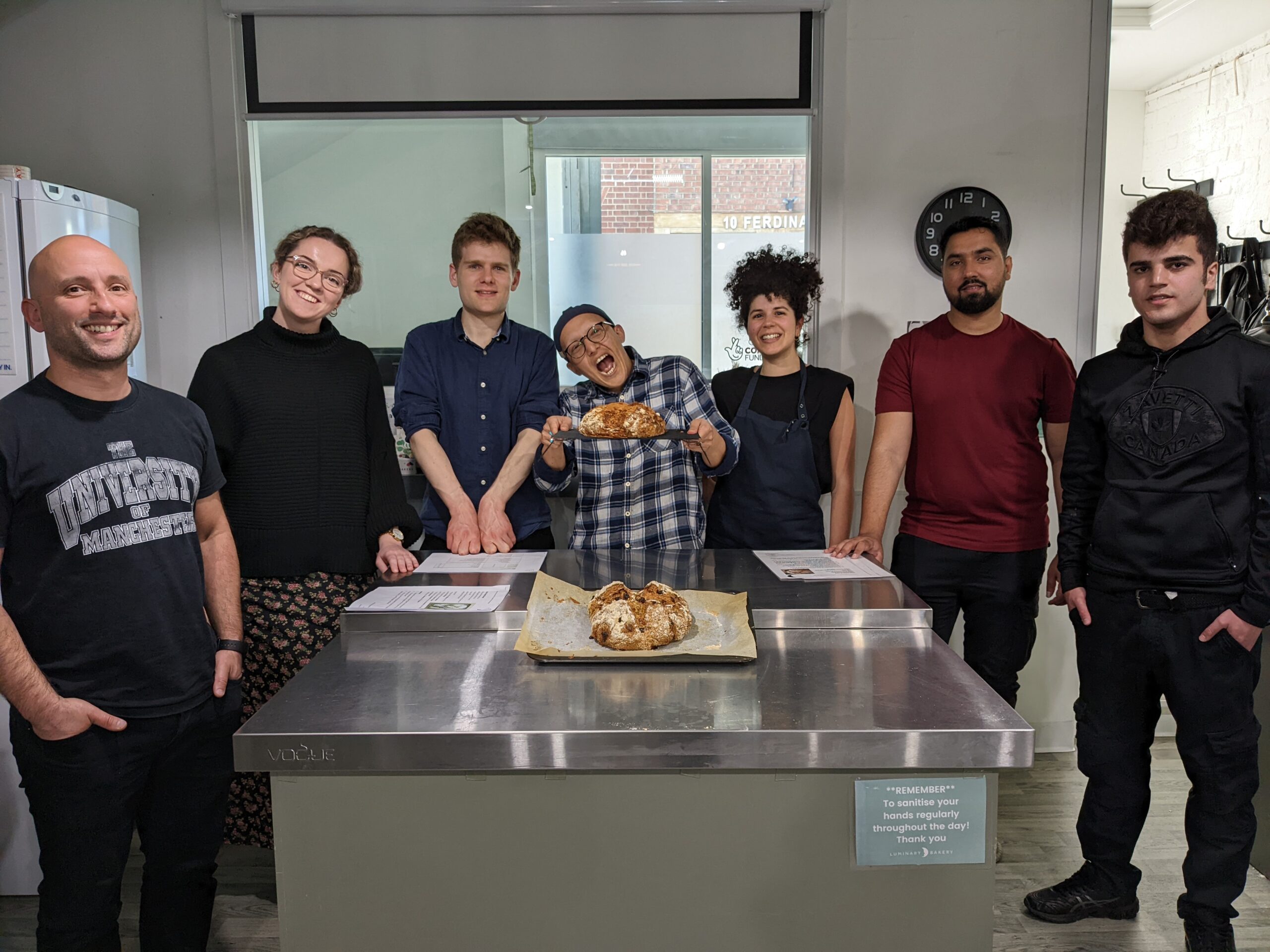 Befrienders and young people stand around a kitchen table, with bread they have cooked together.