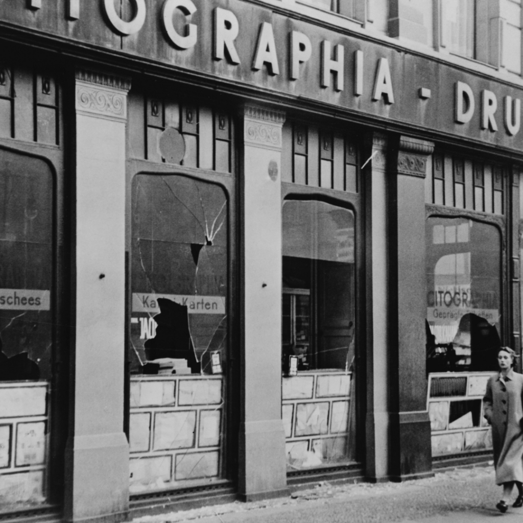 A black and white photo of a shop front damaged during Kristallnacht. Its windows have been smashed.