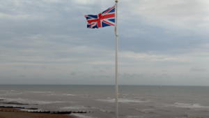 A Union Jack flag flies on a flagpole, ahead of a backdrop of the English channel.